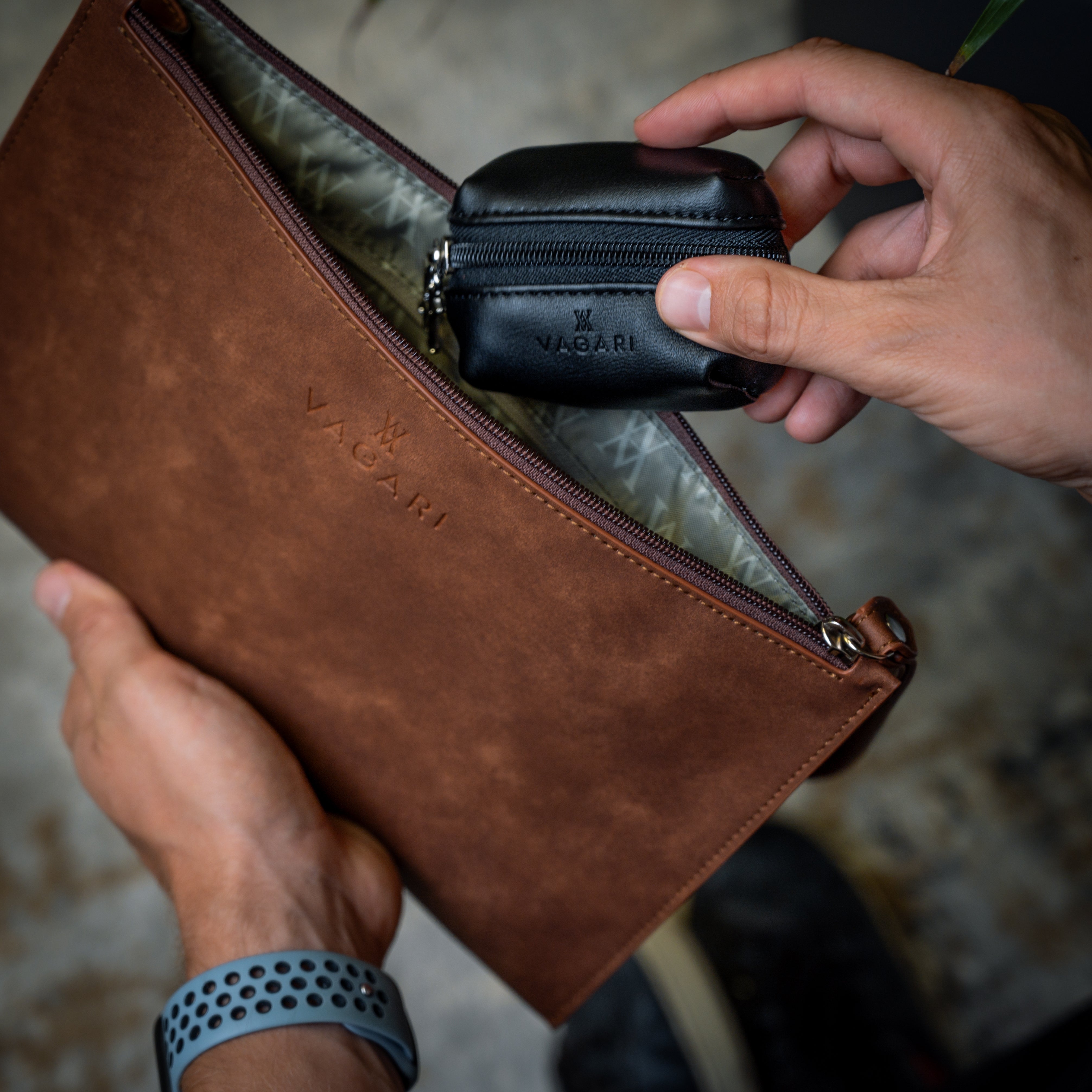 Lifestyle POV of the Geneva Compact Pouch in Cognac, shown in hand with accessory being placed inside.