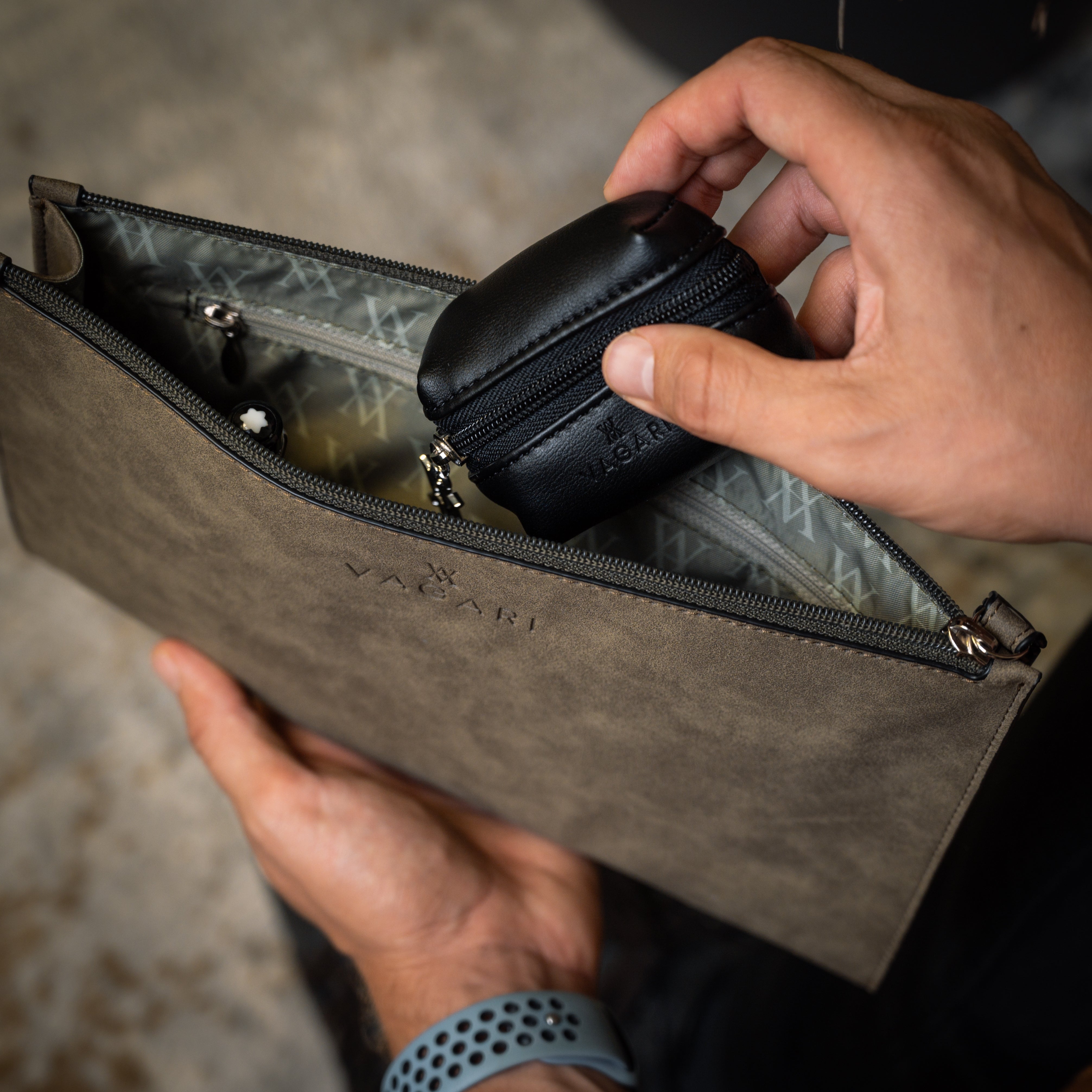 Lifestyle POV of the Geneva Compact Pouch in Olive Drab, shown in hand with earbuds case being placed inside.