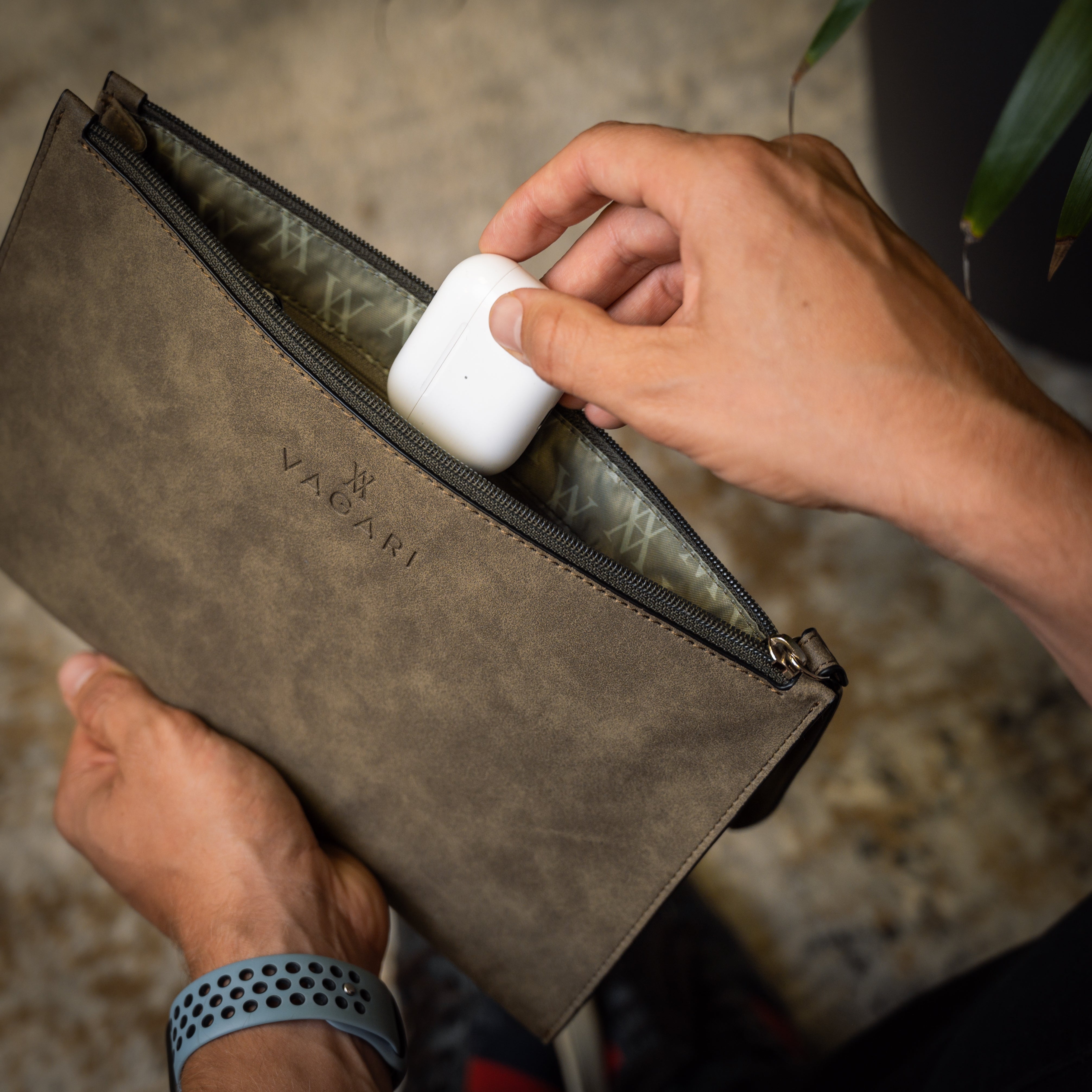 Lifestyle POV of the Geneva Compact Pouch in Olive Drab, shown in hand with AirPods being placed inside.